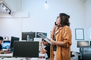 A young Hispanic / Latin entrepreneur at her place of work. She discusses a project she is working on with a client on her smartphone.