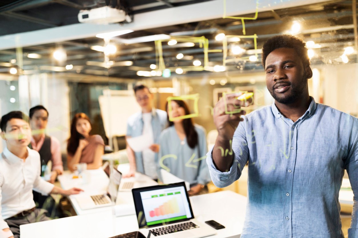 Multi-ethnic group of young entrepreneurs having a business meeting in front of the transparent wipe board in the office