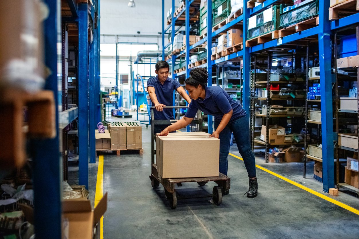 Distribution warehouse workers moving boxes in plant. Man and woman in uniform working in a large warehouse.