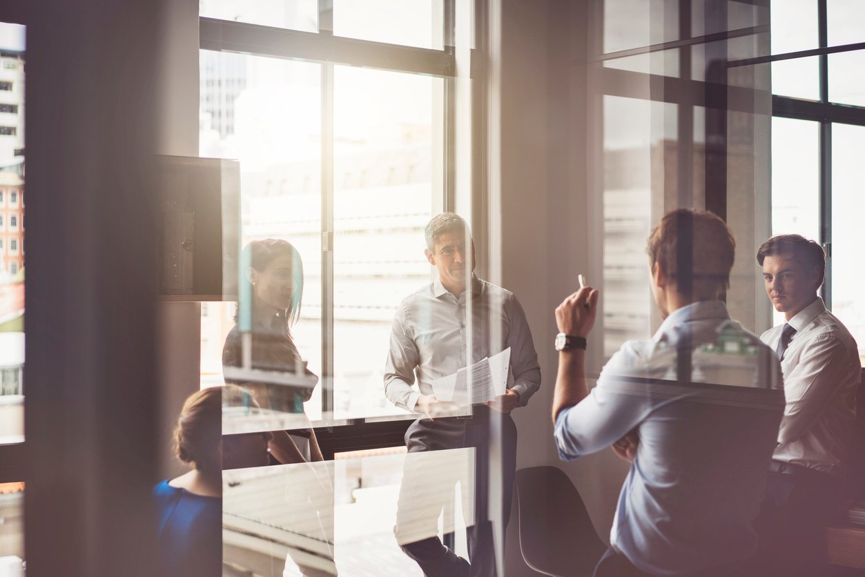 A photo of business people having discussion in board room. Male and female professionals are seen through glass. They are working in office.